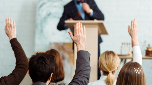 back_view_of_buyers_raising_hands_to_auctioneer_during_auction
